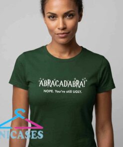 Funny You're Still Ugly Abracadabra T-Shirt, humorous magic quote graphic tee, cotton short sleeve shirt for casual streetwear fans, available in black and white.